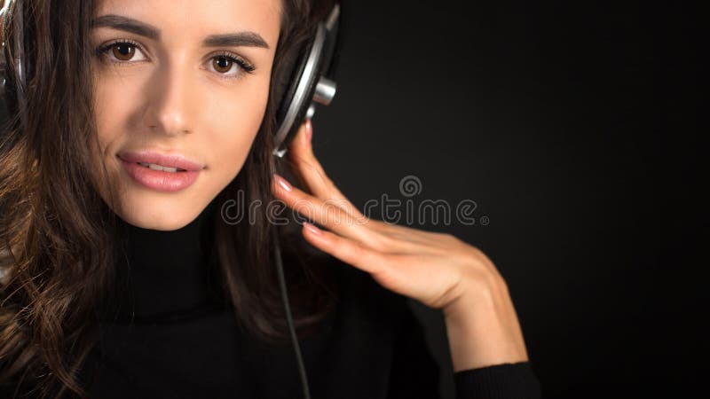 Beautiful enjoying young woman listening the music in wireless headphone with closed eyes on dark black background