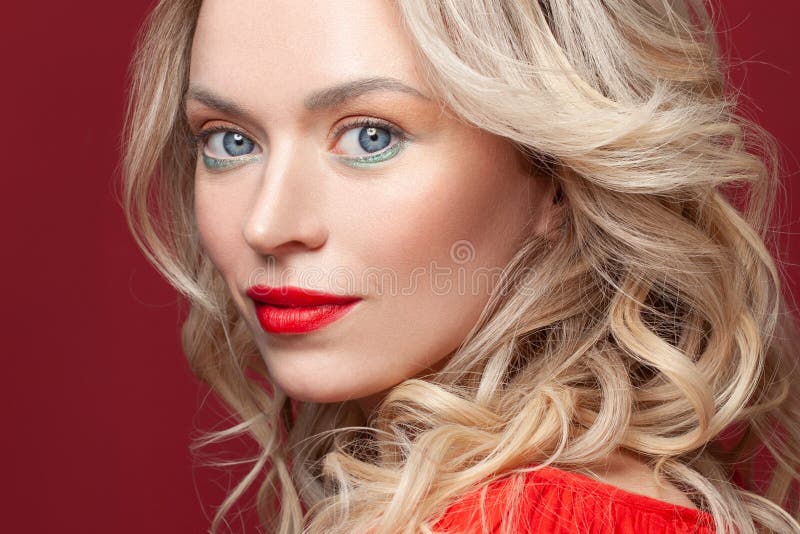 Beautiful face, studio portrait. Nice woman with blonde curly hair and makeup on red background royalty free stock photo