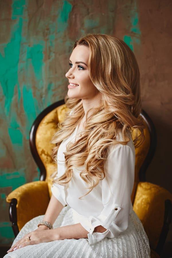 Beautiful fashionable blond model girl with blue eyes is sitting in the vintage armchair, indoors stock image Beautiful fashionable blond model girl with blue eyes is sitting in the vintage armchair, indoors stock image