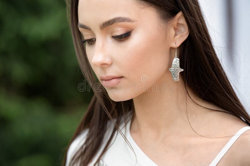 Beautiful fashionable girl in stylish jewelry. The model poses in the street with flowering trees. Spring