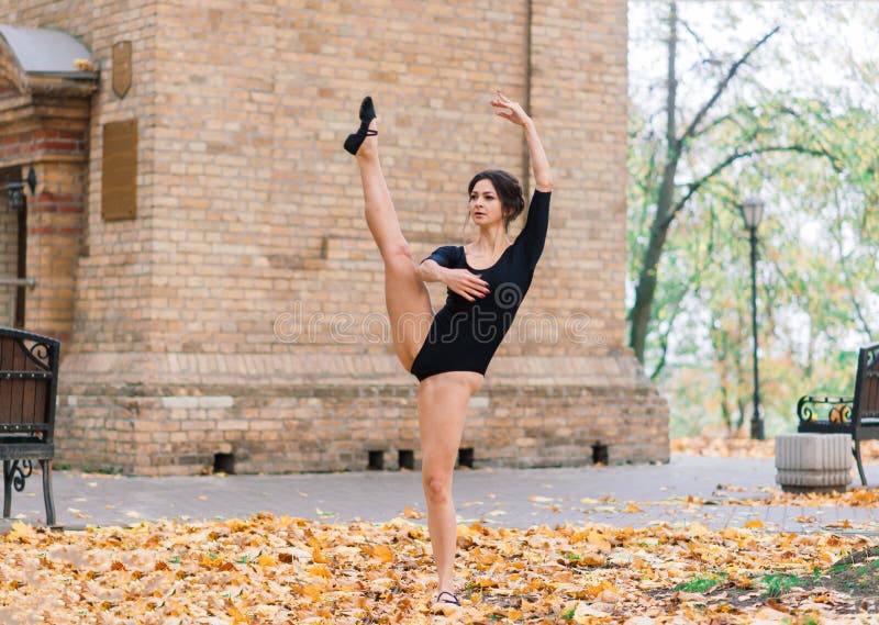 Beautiful female, ballerina, athlete in black bodysuit training in the park