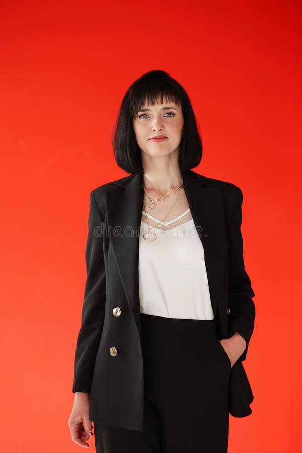 Beautiful female brunette business woman CEO in a black suit, isolated on red background, standing confidently with arms