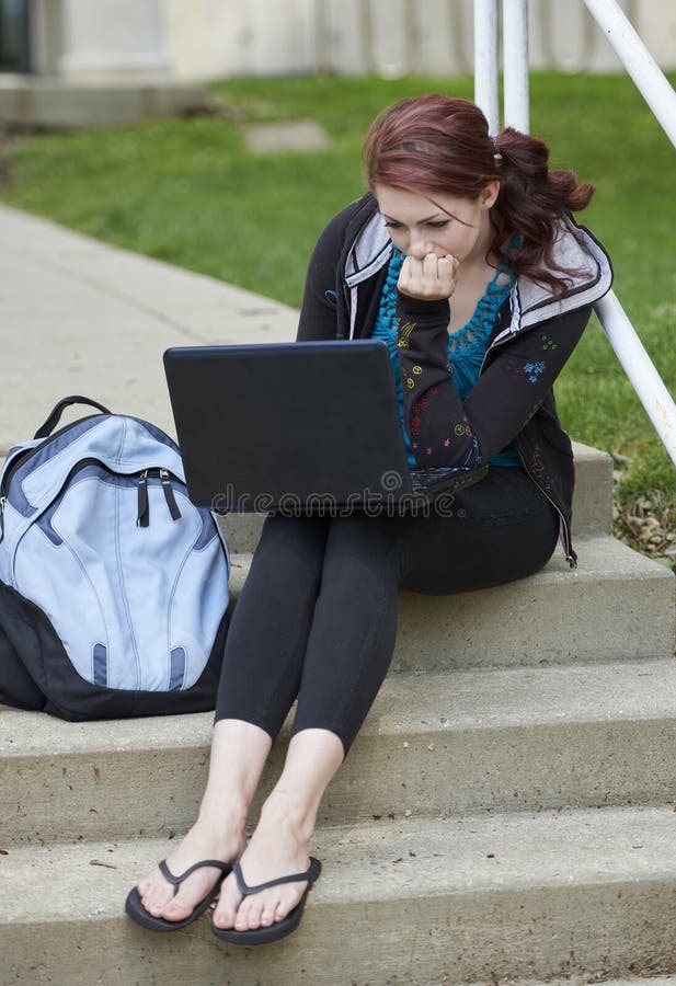 Beautiful female student, with red hair, wearing backpack on campus - sitting on stairs with laptop computer. Beautiful female student, with red hair, wearing backpack on campus - sitting on stairs with laptop computer