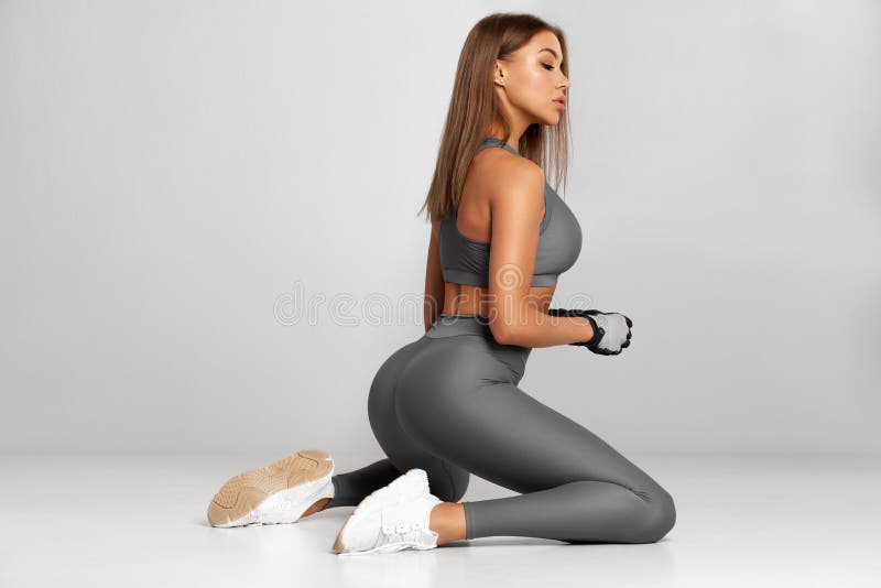 Beautiful fitness woman. in leggings. athletic girl sitting, isolated on the gray