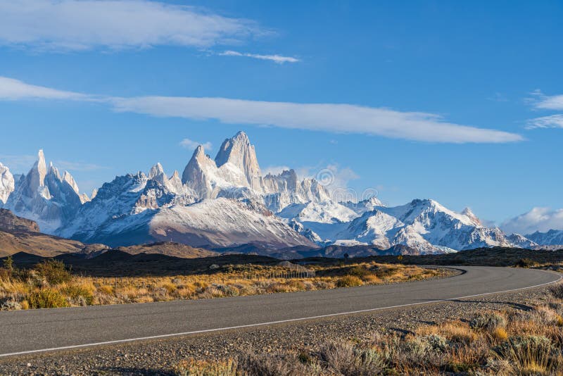 Beautiful Fitz Roy and Cerro Torre peak snow mountain in the morning blue sky with golden yellow grass beside the asphalt road