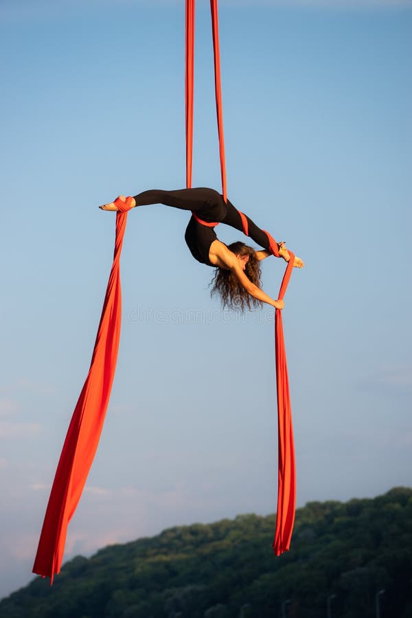 Beautiful And Flexible Female Circus Artist Dancing With Aerial Silk On A Sky Background Stock