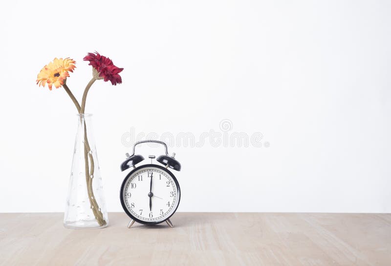 Beautiful flower in vase and alarm clock on wood table.