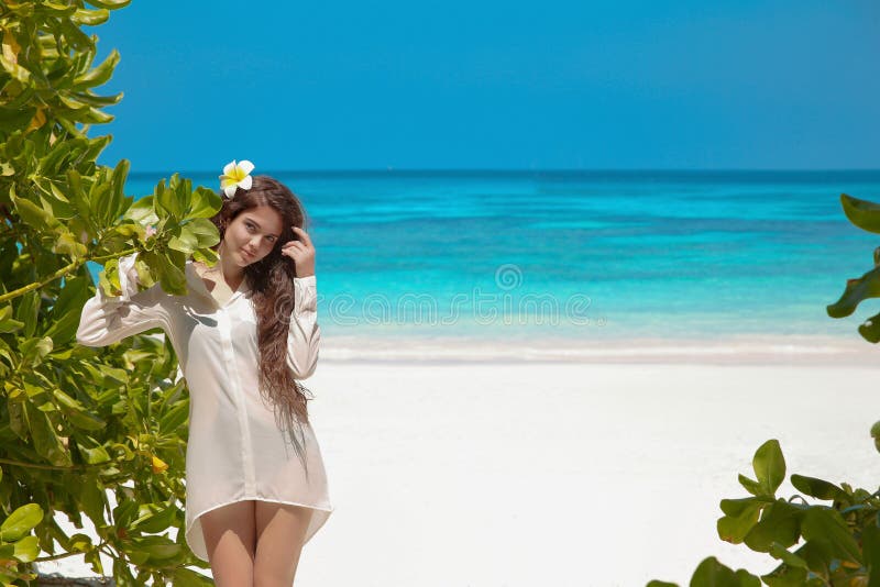 Beautiful free woman enjoying on exotic beach in summer by tropical blue water. Attractive girl with long hair sunbathing and res