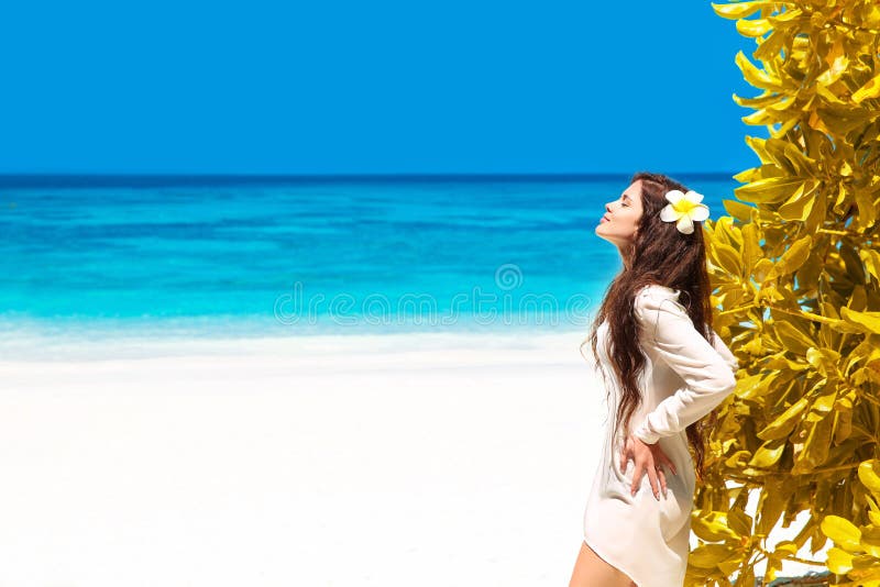 Beautiful free woman enjoying on exotic beach in summer by tropical blue water. Attractive girl with long hair sunbathing and res