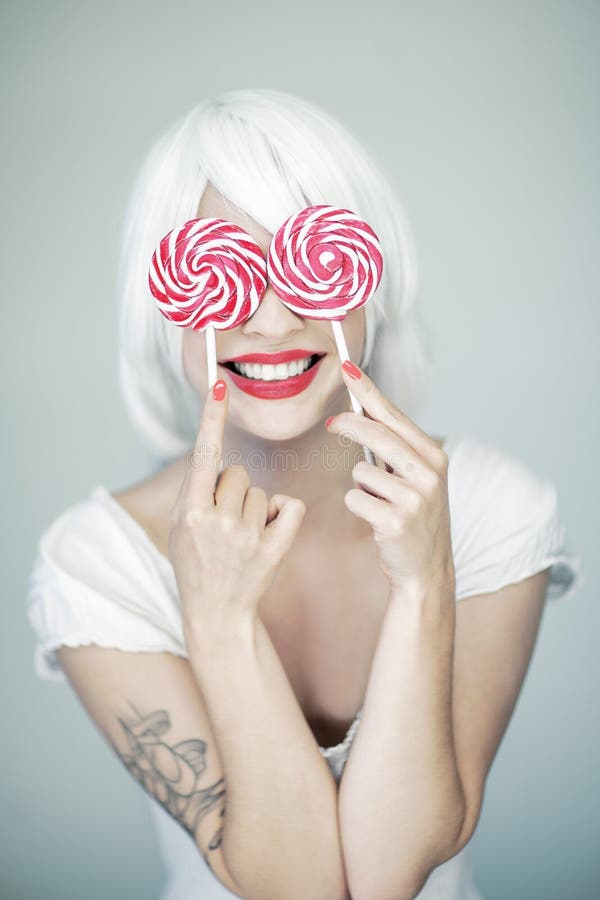 Beautiful funny woman in white and perfect pink makeup holding two swirl lollipops royalty free stock photography Beautiful funny woman in white and perfect pink makeup holding two swirl lollipops royalty free stock photography
