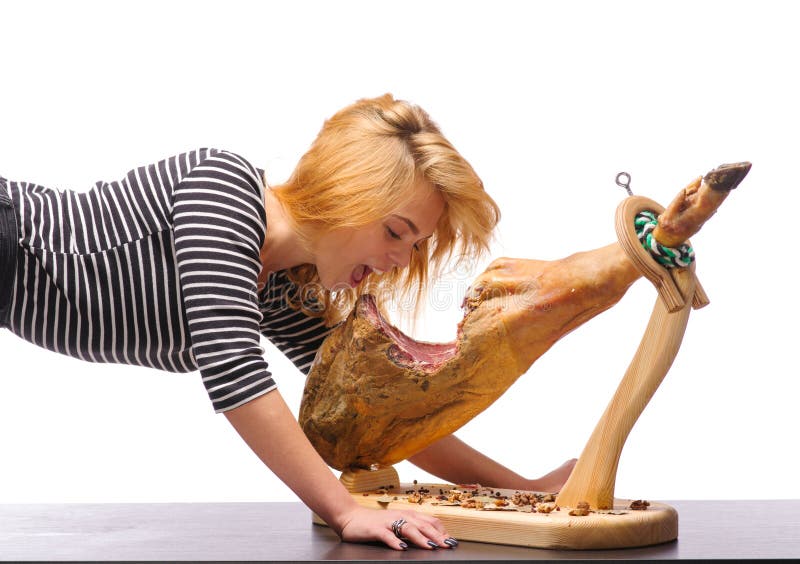 A beautiful girl is biting a whole jamon on a wooden stand.