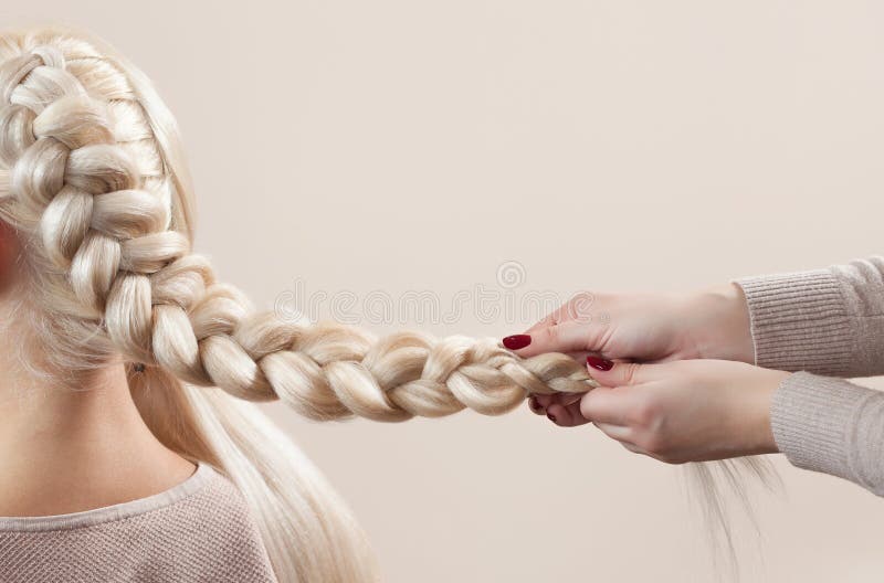 Beautiful girl with blonde hair, hairdresser weaves a braid close-up