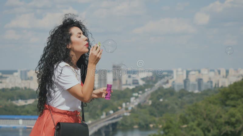 Beautiful girl blows bubbles at city background