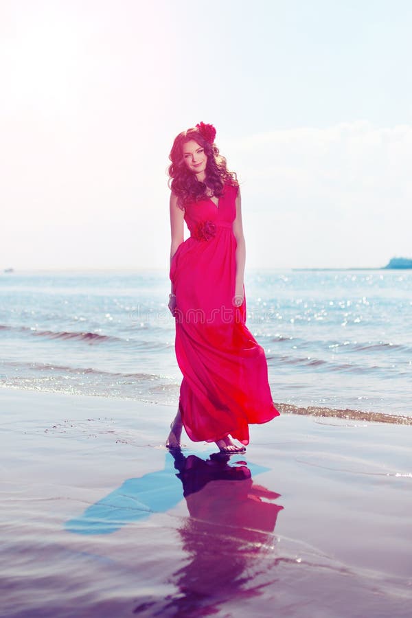 Beautiful girl in a bright red dress by the sea. Against the background of the summer lanshaft. Young romantic woman in