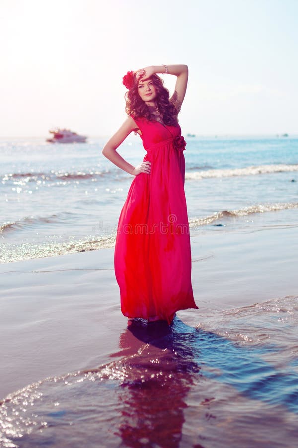 Beautiful girl in a bright red dress by the sea. Against the background of the summer lanshaft. Young romantic woman in