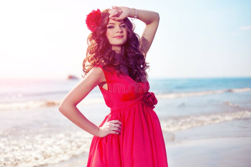 Beautiful girl in a bright red dress by the sea. Against the background of the summer lanshaft. Young romantic woman in