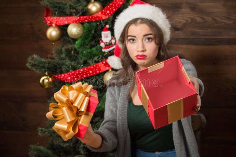 Beautiful girl demonstrating empty box of present near New Year tree