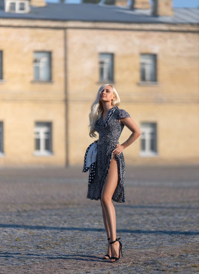 Beautiful girl in the dotted dress with perfect legs and shoes with high heels posing outdoor on the city square