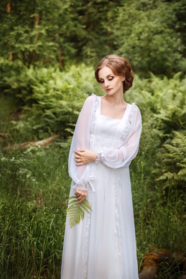 Beautiful girl on the edge of the forest in a long white dress