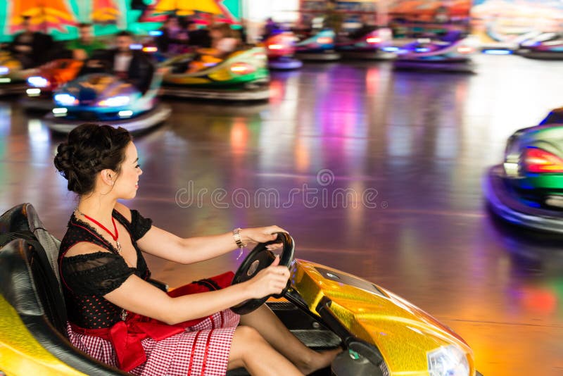 Beautiful girl in an electric bumper car at amusement park. Beautiful girl in an electric bumper car in amusement park in typical German Dirndl dress with bright royalty free stock photos Beautiful girl in an electric bumper car at amusement park. Beautiful girl in an electric bumper car in amusement park in typical German Dirndl dress with bright royalty free stock photos
