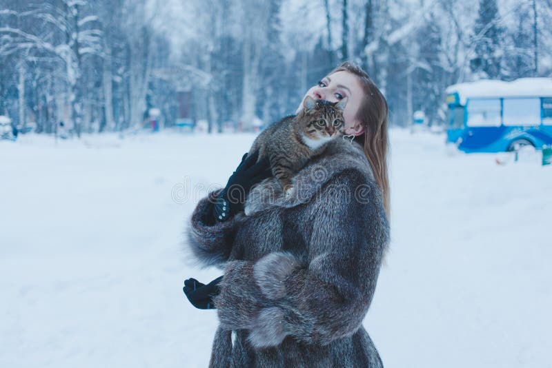 Girl in a fur coat holding a cat in her arms against the background of a winter forest royalty free stock image Girl in a fur coat holding a cat in her arms against the background of a winter forest royalty free stock image