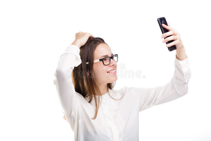 Beautiful girl in glasses and a white shirt takes a picture of herself on the camera phone, selfie on white isolated background