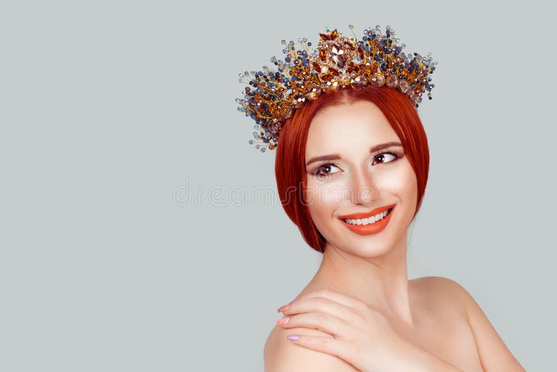 Beautiful girl in a golden crown on grey background, looking to the side hand on shoulder smiling happy pretty woman with crystal