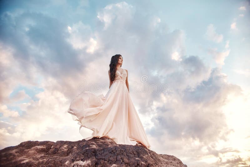 Beautiful girl in a light summer dress beige walks in the mountains. Light dress flutters in the wind, blue summer sky. Fabulous
