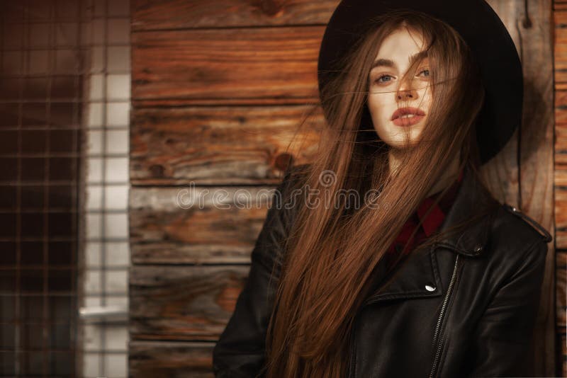 Beautiful girl with long hair and black hat, stands on the background of vintage old wooden house royalty free stock photography Beautiful girl with long hair and black hat, stands on the background of vintage old wooden house royalty free stock photography