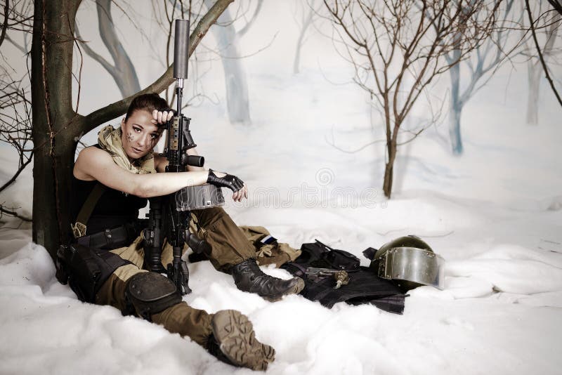 The beautiful girl in a military uniform with the weapon sits royalty free stock photo