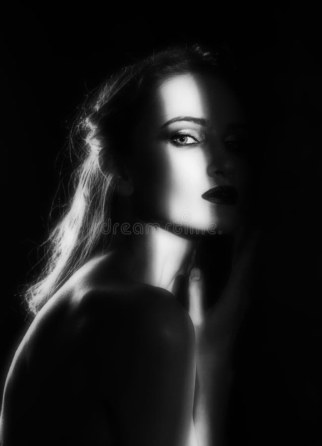 Beautiful girl model with red lips make up and naked shoulders in the shade, with a lit silhouette and a strip of light