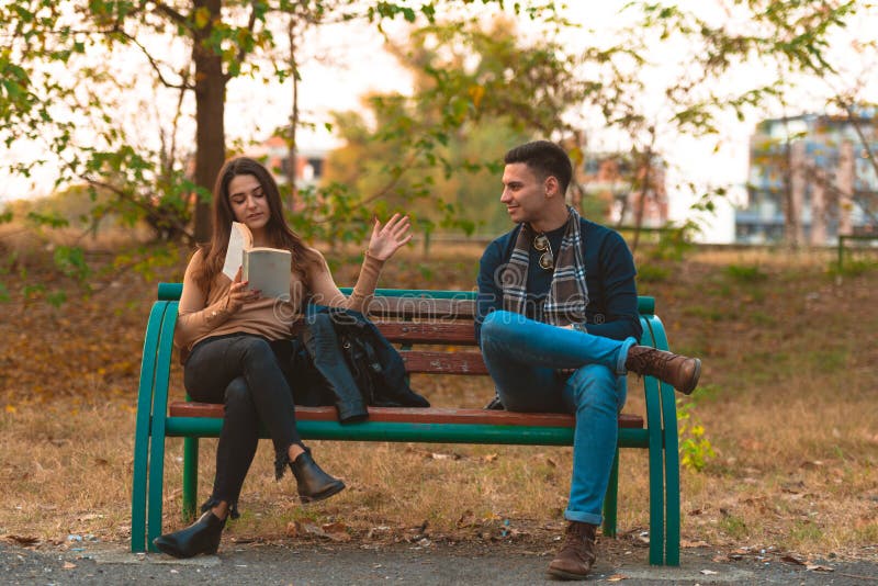 A beautiful girl is reading a book while handsome man is trying to get her attention