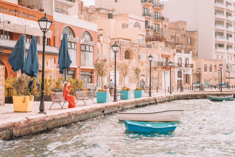 Beautiful girl in a red dress sitting by the boats docked on the island of Malta.