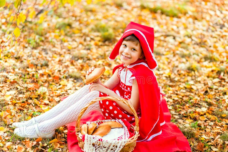 Beautiful girl in a red dress sitting on yellow foliage in autumn