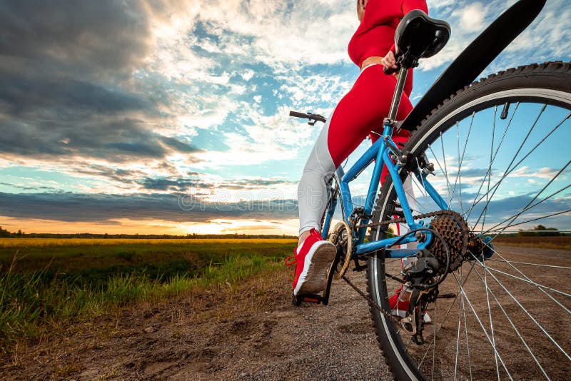 Beautiful girl in a red sports suit on a bicycle on a sunset background. The concept of a healthy lifestyle, sports training