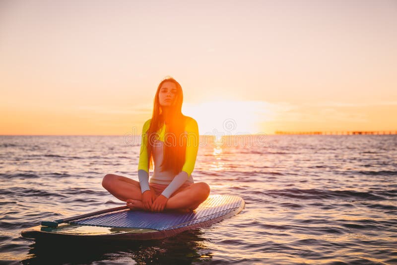 Beautiful girl relaxing on stand up paddle board, on a quiet sea with warm sunset colors.