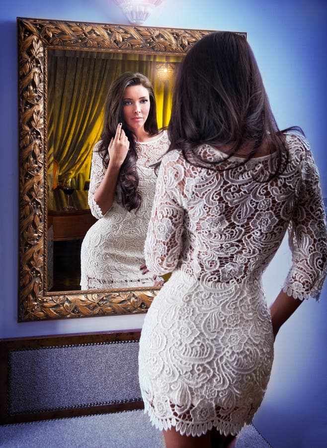 The beautiful girl in a short white dress looking into mirror