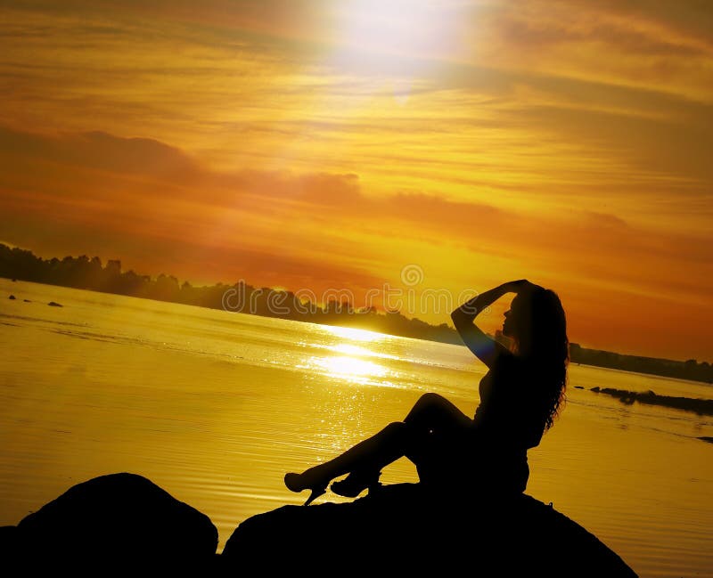 Beautiful girl sits on stone on sundown