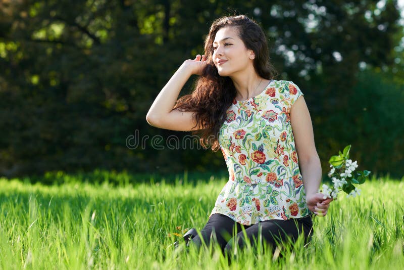 Beautiful girl sitting on a glade in the park, bright sun and sh