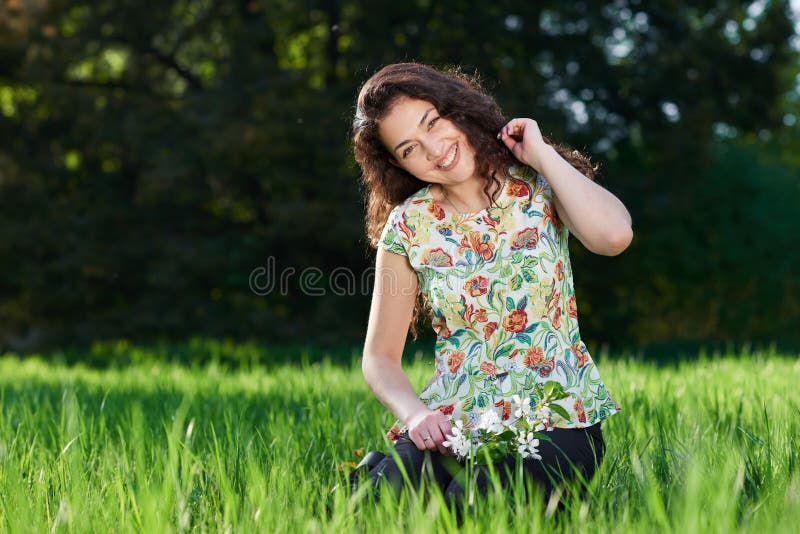 Beautiful girl sitting on a glade in the park, bright sun and shadows on the grass