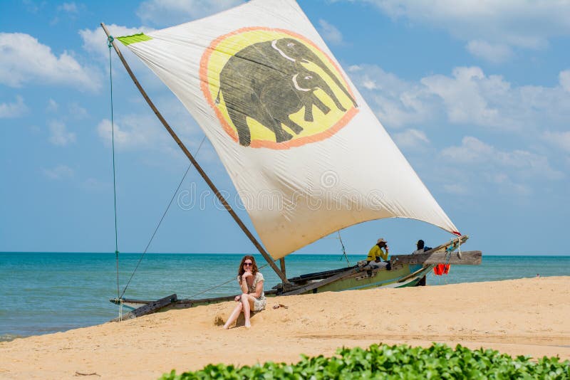 Beautiful girl sitting near the sailing boat on the beach