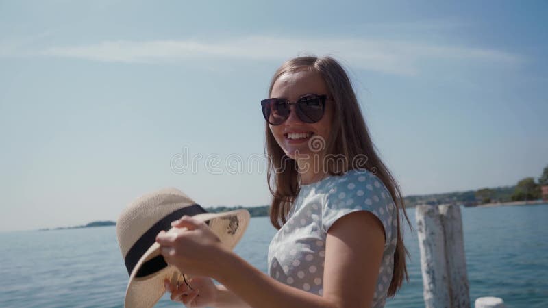 Beautiful girl in sunglasses takes off her straw hat and covers camera with her