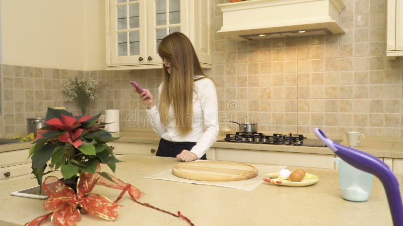Beautiful girl uses phone at the kitchen