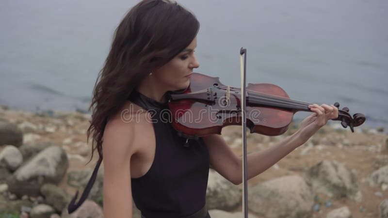 Beautiful girl with violin. Young violinist in dress plays at sea background