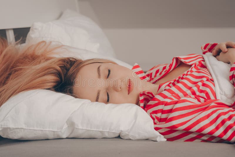 A Beautiful Girl On A White Bed In Red Striped Pajamas Is Sleeping