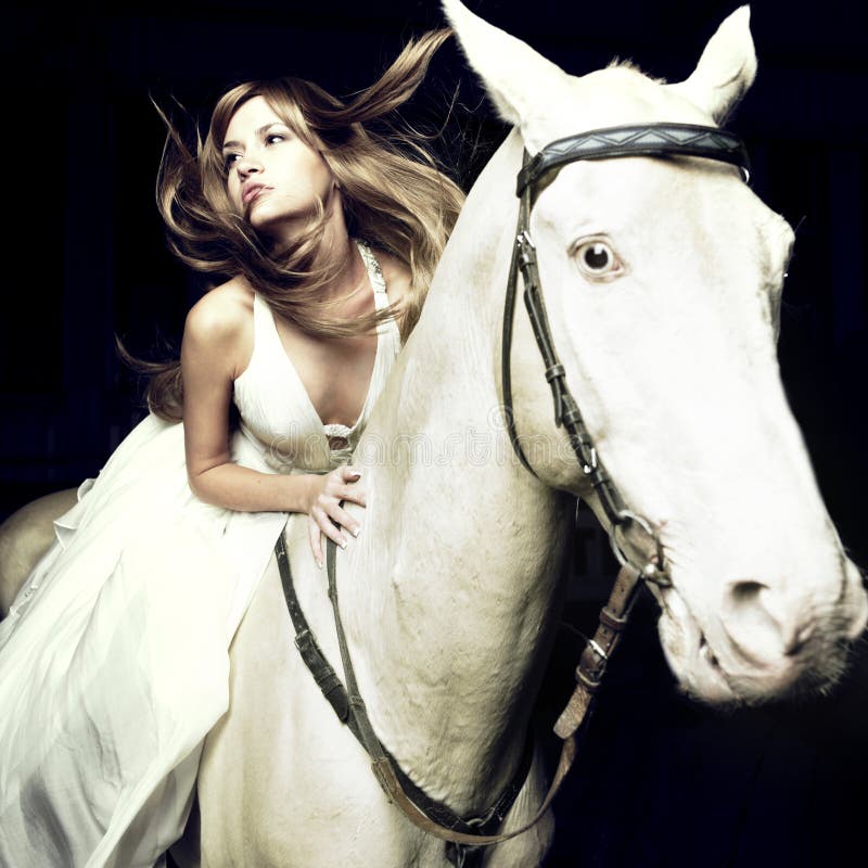 Bella bionda in abito bianco su un cavallo bianco.