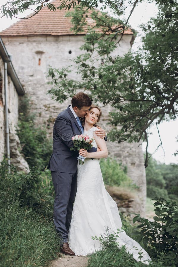 Beautiful gorgeous bride and groom walking in sunny park and kissing. happy wedding couple hugging in green garden at old castle.