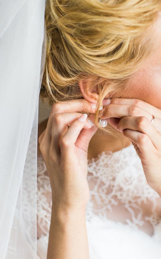 Beautiful gorgeous bride putting on luxury earrings stock photography