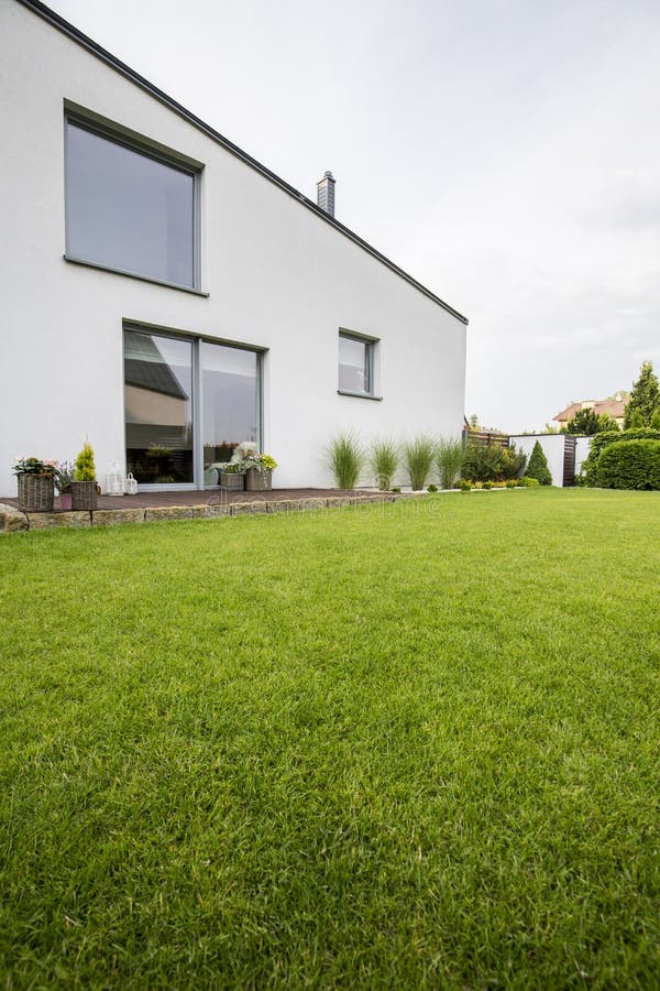 Beautiful green lawn in the backyard of a modern residential house with plants on a wooden terrace and big windows stock image Beautiful green lawn in the backyard of a modern residential house with plants on a wooden terrace and big windows stock image