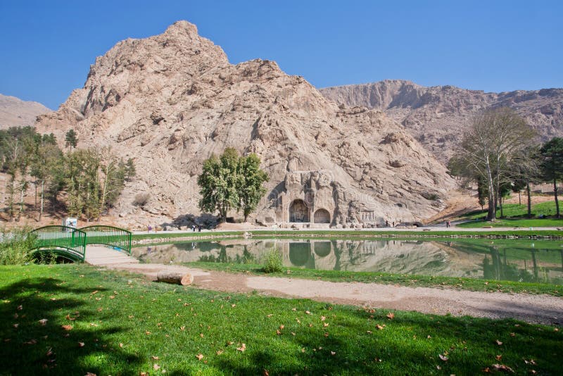 Beautiful green park with lake, montains and historical site - Arches of Taq-e Bostan, Iran.